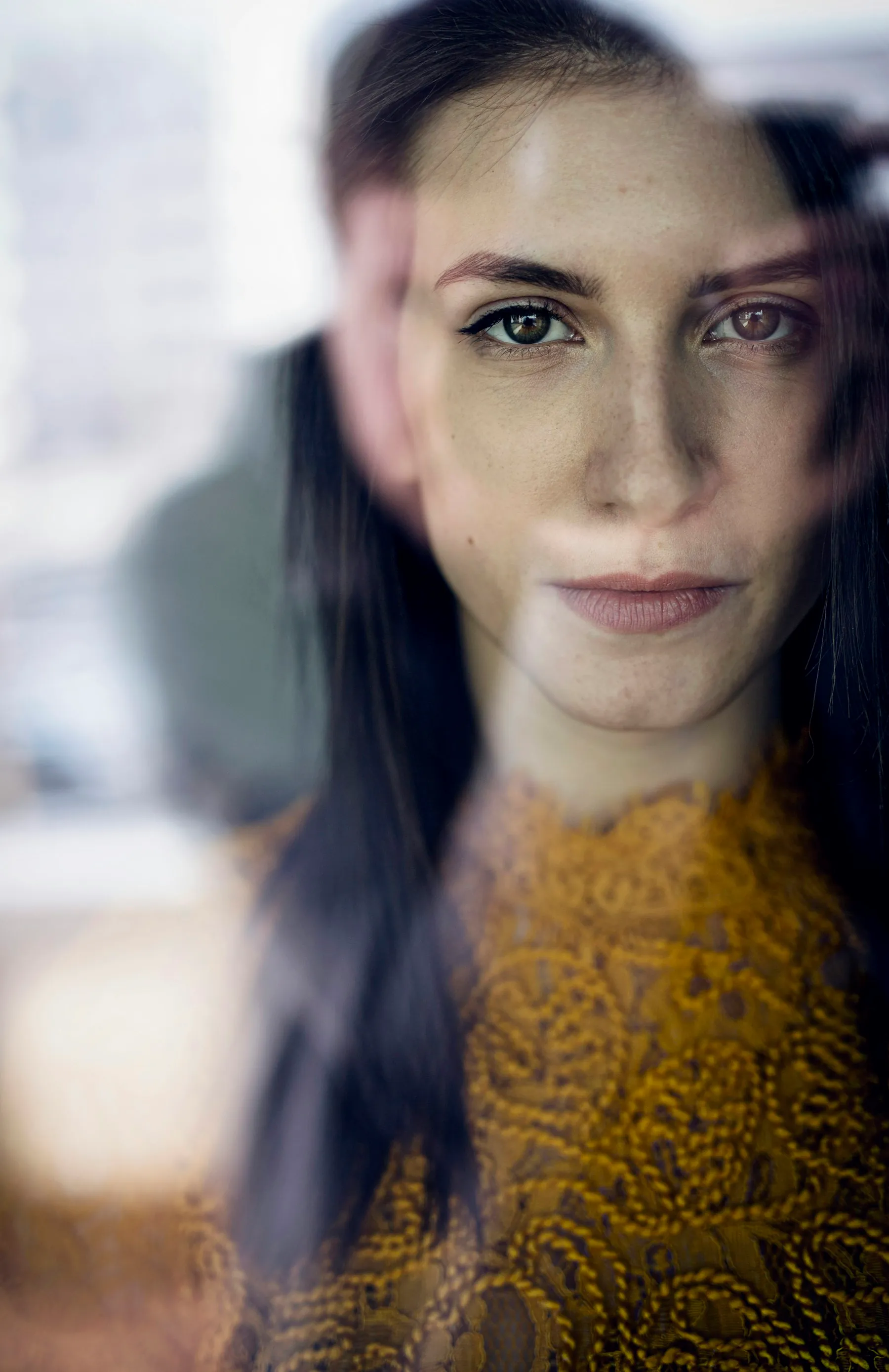 A woman with long dark hair looking calmly at the camera through soft, out-of-focus light