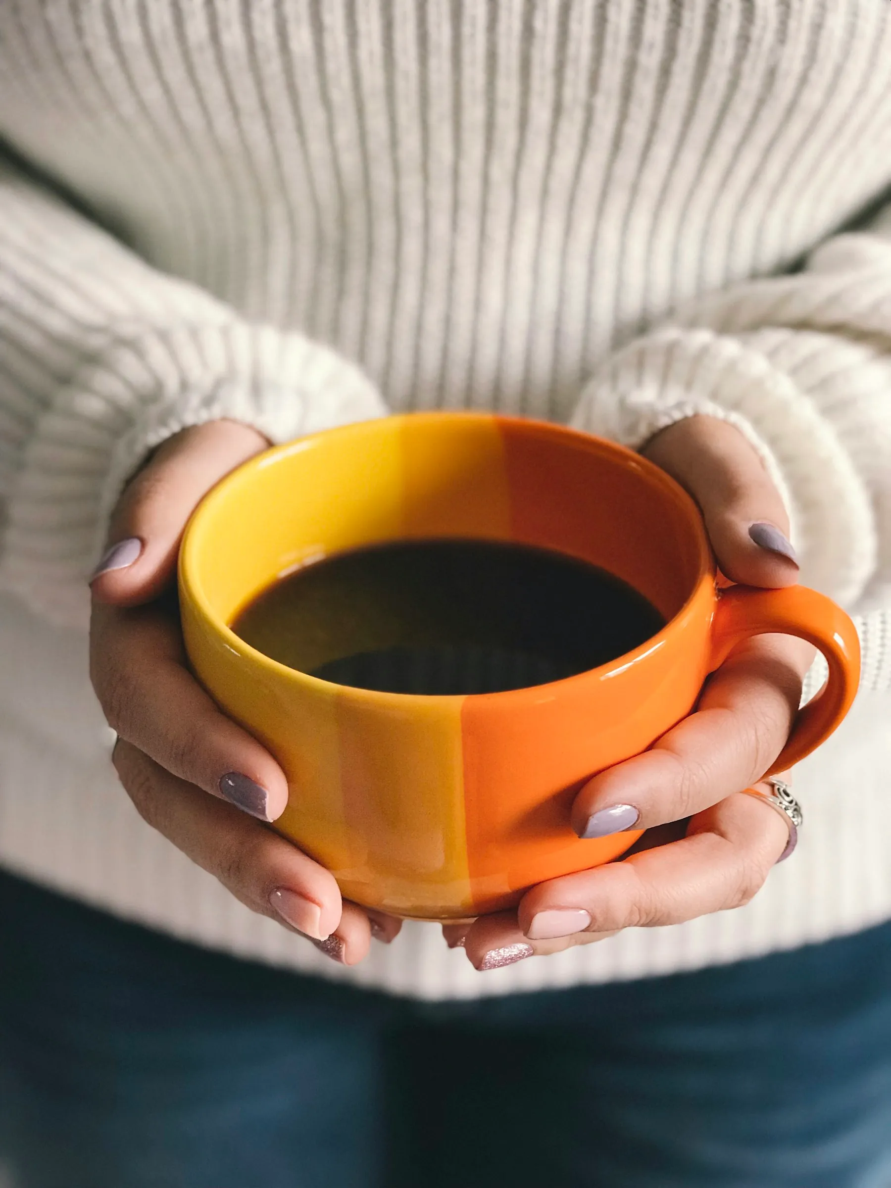 Two hands wrapped around a warm orange mug against a cream knitted jumper